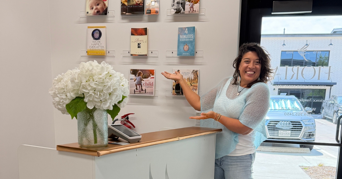 Me Ra Koh gesturing toward her book wall in her Frisco, Texas studio, sharing her story of learning to rebuild confidence after trauma.